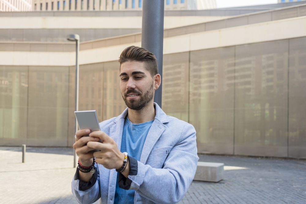 Man in blazer leaning on pole outside talking on video call