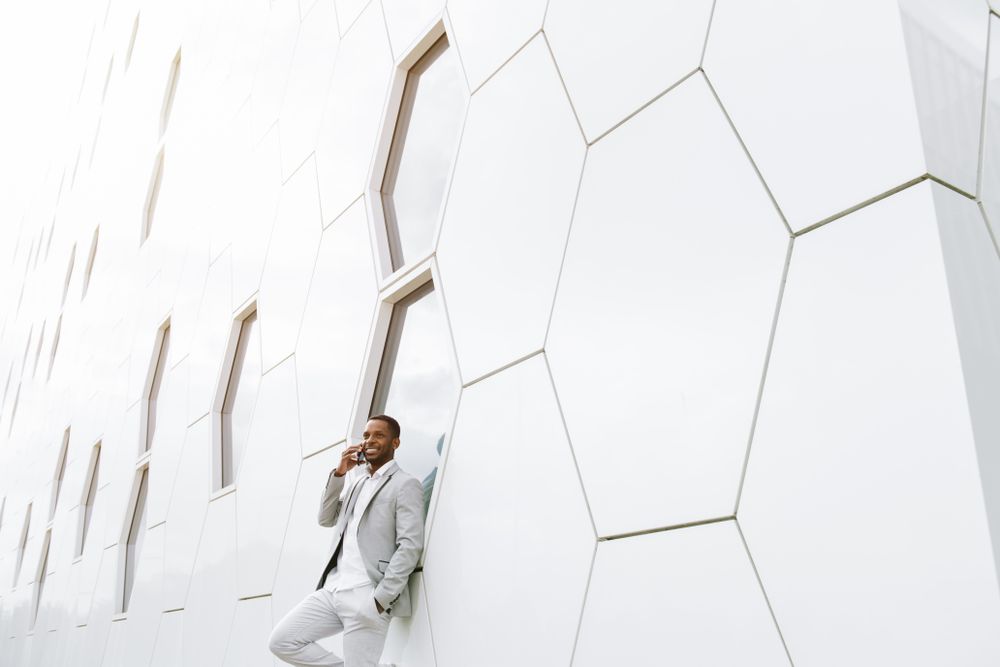 Elegant Black man talking smartphone leaning on geometrical wall
