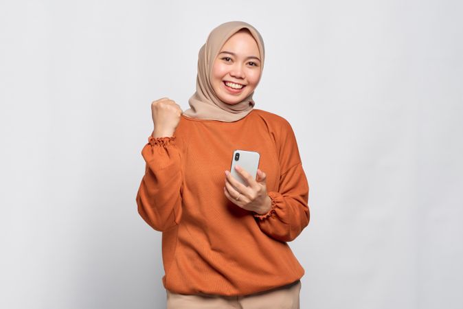 Muslim woman smiling holding smart phone and fist up like she won
