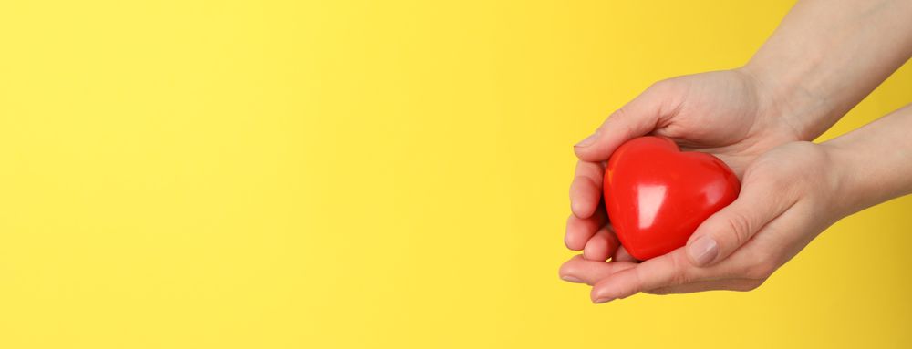 Female hands hold heart on yellow background. Health care, organ donation