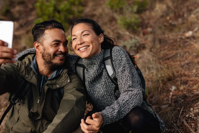 Man and woman resting on mountain trail taking selfie
