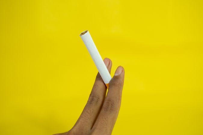 Hand holding cigarette against yellow wall