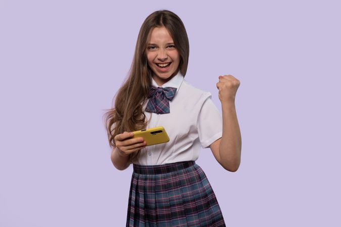 Girl celebrating victory while holding smartphone.