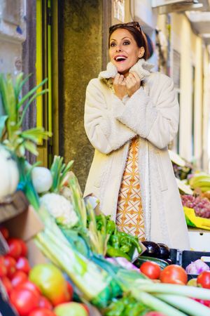 Smiling woman standing by colorful ripe fruits and vegetables in shop