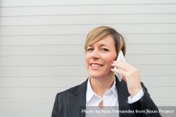 Happy businesswoman speaking on cell phone in front of wall 5oroG0