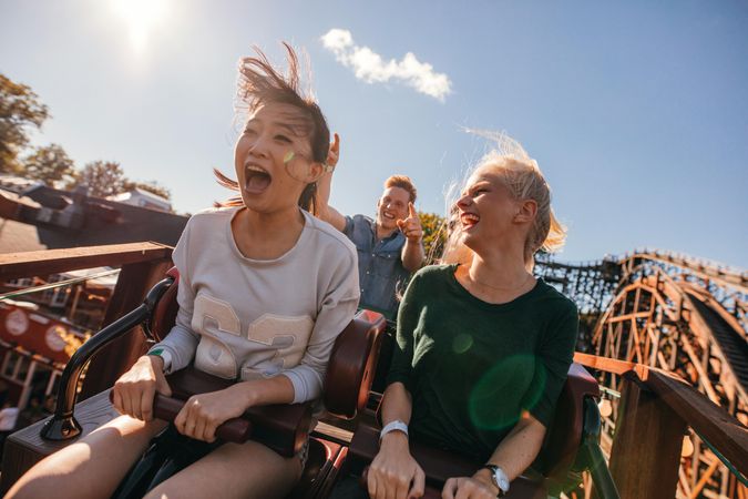 Young friends on yelling on thrilling roller coaster ride