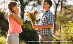 Happy boy and girl standing in a park with the boy giving a bouquet of flowers 5lW160