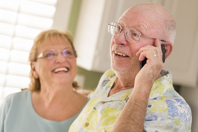 Older Adult Husband on Cell Phone with Wife Behind