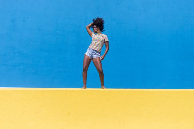 Black woman posing atop bright yellow and blue wall