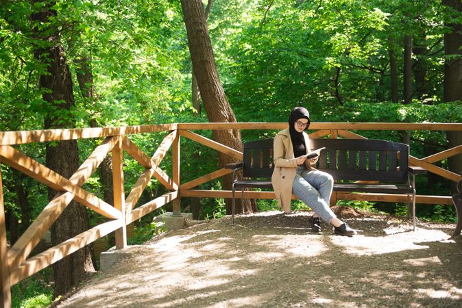 Middle Eastern woman sitting on park bench with book on sunny day