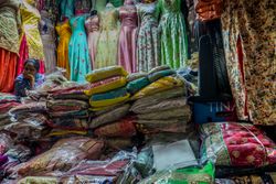 Colorful fabrics and dresses being sold by a woman in a market