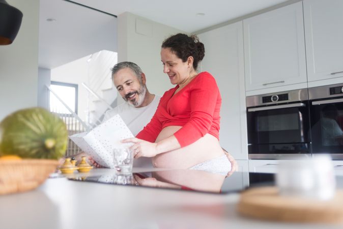 Pregnant woman and husband reading recipe book in bright kitchen