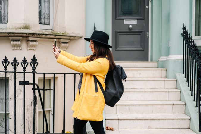 Stylish woman using smartphone near house on street