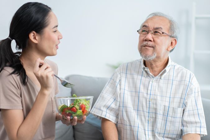 Older man smiling while eating tasty food from beloved daughter