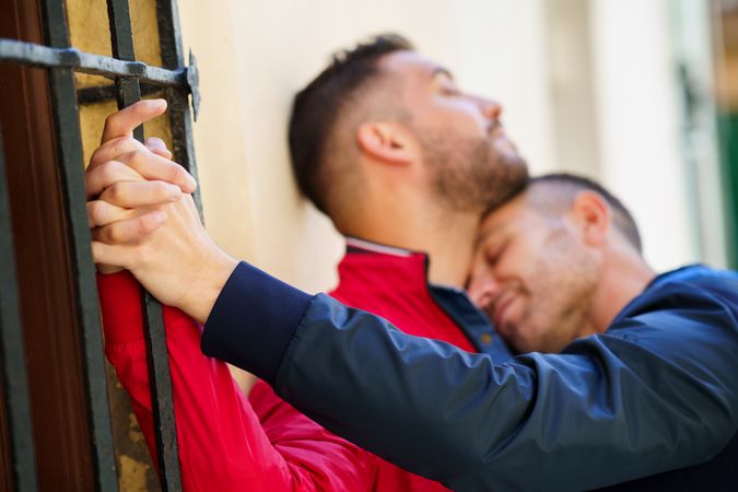 Two men embracing lovingly against building