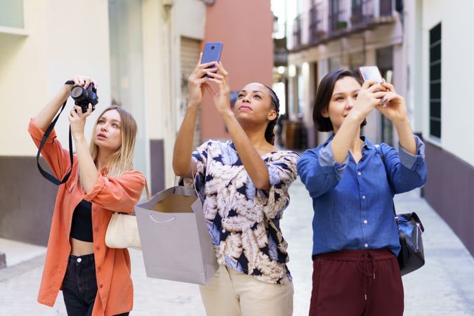 Three women looking up and taking pictures with their phone in narrow lane