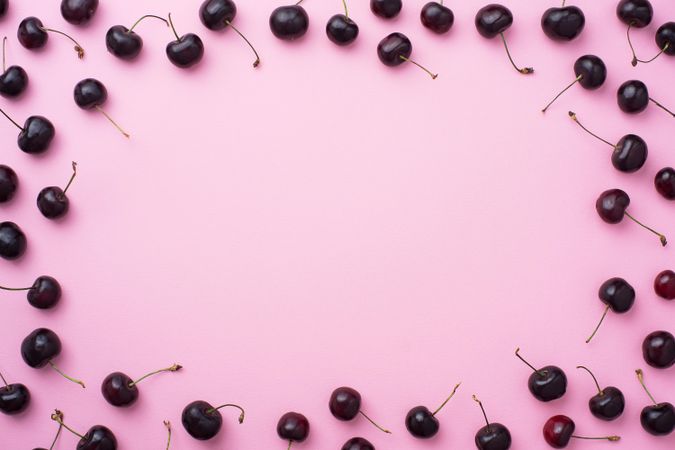 Many cherries scattered over a pink background blank space in the center