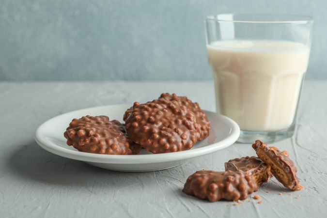 Glass of milk and plate with chocolate cookies on grey table against light background