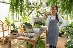 A young woman in an apron holds a welcome open sign in the greenhouse.
