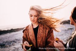 Young woman’s long hair blowing in the wind with her friend looking on DbG3Ab