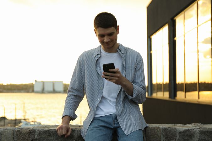 Young man uses a phone outdoor. Writing a message