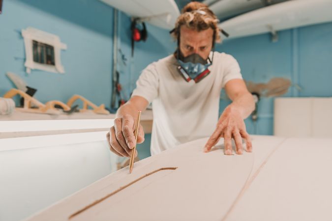 Man in respirator measuring surf board in workshop