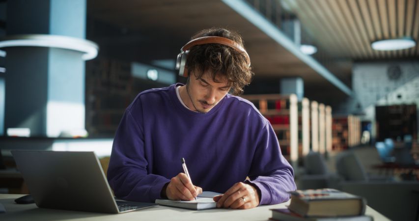 Thoughtful Young Student Preparing for Class, Doing Homework on a Laptop Computer. Freelance Journalist Working on an Article in a Public Library with Modern Simple Interior
