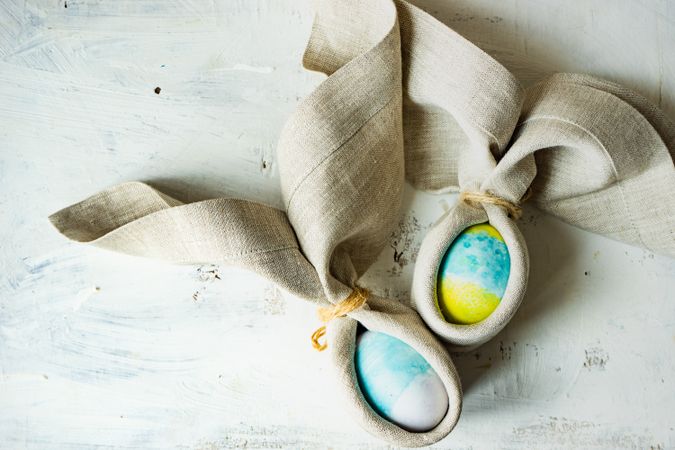Easter eggs wrapped with rabbit ears with napkin with nest on light table