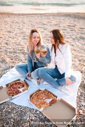 Two mature women eating pizzas and drinking wine sitting on sand beach 0vmOGb