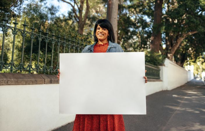 Smiling brunette woman holding a blank placard outdoors