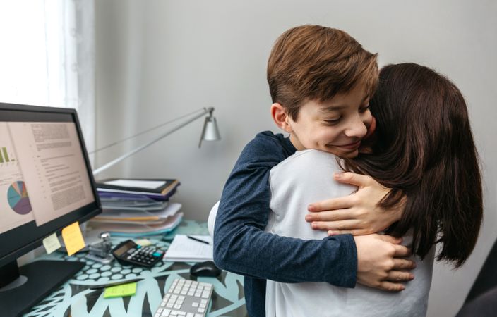 Mother and son hugging while she telecommutes