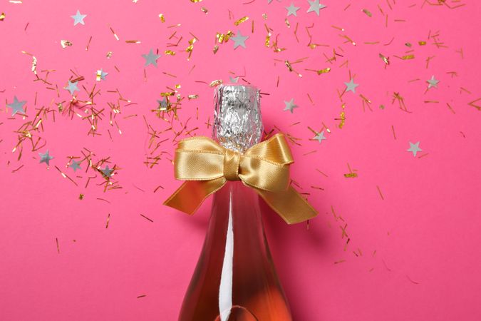 Champagne bottle with bow and glitter on pink background, close up
