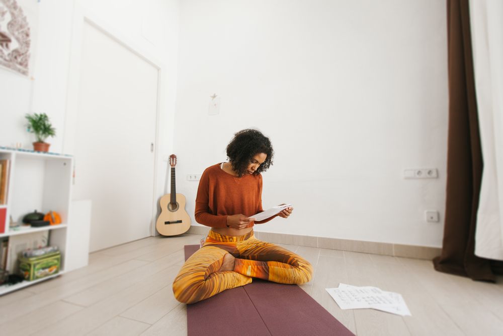 Sportive woman sitting with legs crossed on floor studying routine paper