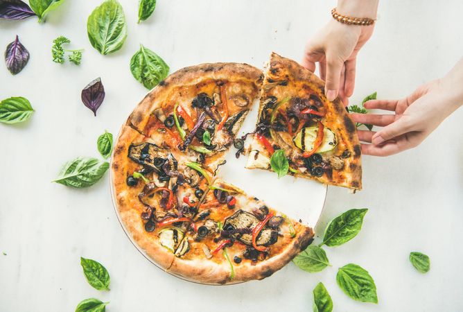 Quartered wood fired vegetable pizza with hand taking slice