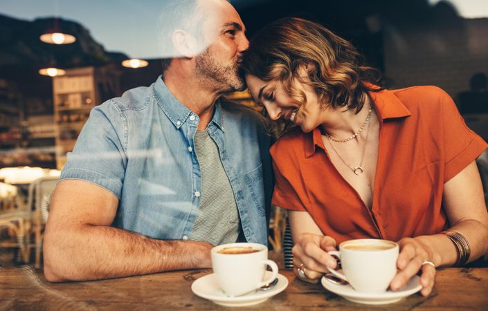 Man kissing forehead of his woman sitting at cafe