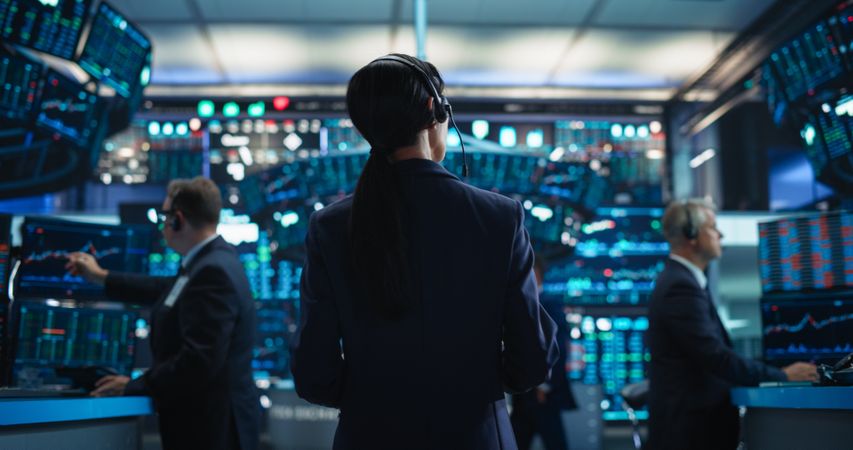 Female Investment Banker Wearing Headphones and Using a Tablet Computer with Financial Market Analytics Data.