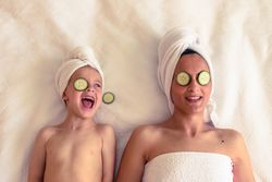 Cheerful kid with mother with cucumber on eyes