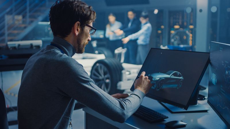 Professional Automotive Graphic Designer is Working on Concept Car Render with a Stylus Pen in a High Tech Innovative Laboratory with a Prototype Car Chassis.
