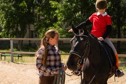 Instructor discusses technique with young rider during equestrian lesson.
