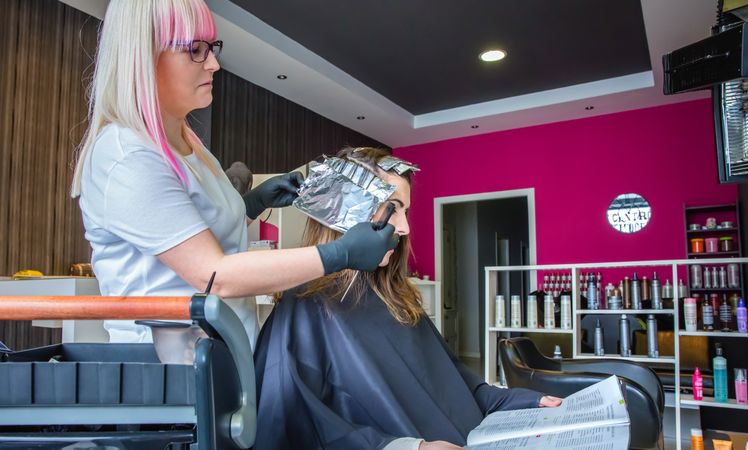 Hairdresser with pink hair working with client in salon with pink wall