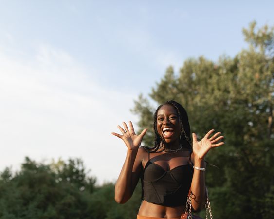 A young Black woman, with braids in her hair, gesticulates and gets excited, during a walk in the park at sunset