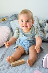 Cheerful toddler sitting on bed near toy block at home