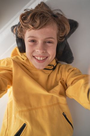 Cheerful child in headphones listening to music and taking selfi