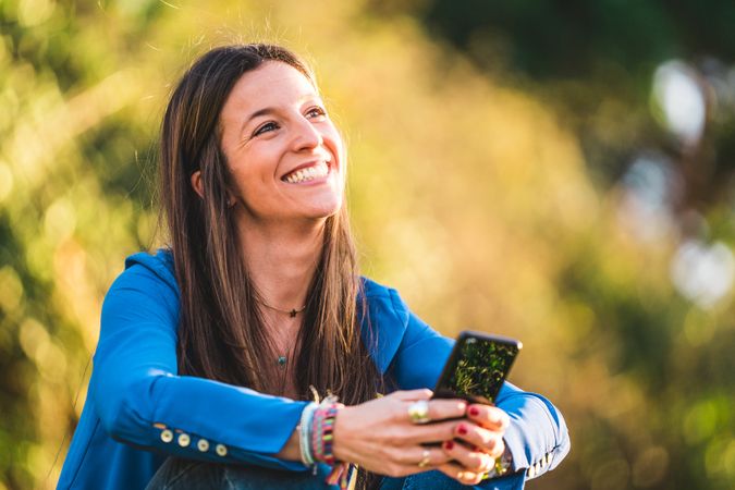 portrait of young woman using smartphone sitting on grass in park
