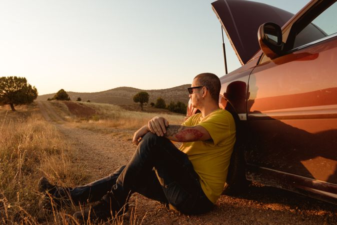 Man leaning in broken car in countryside