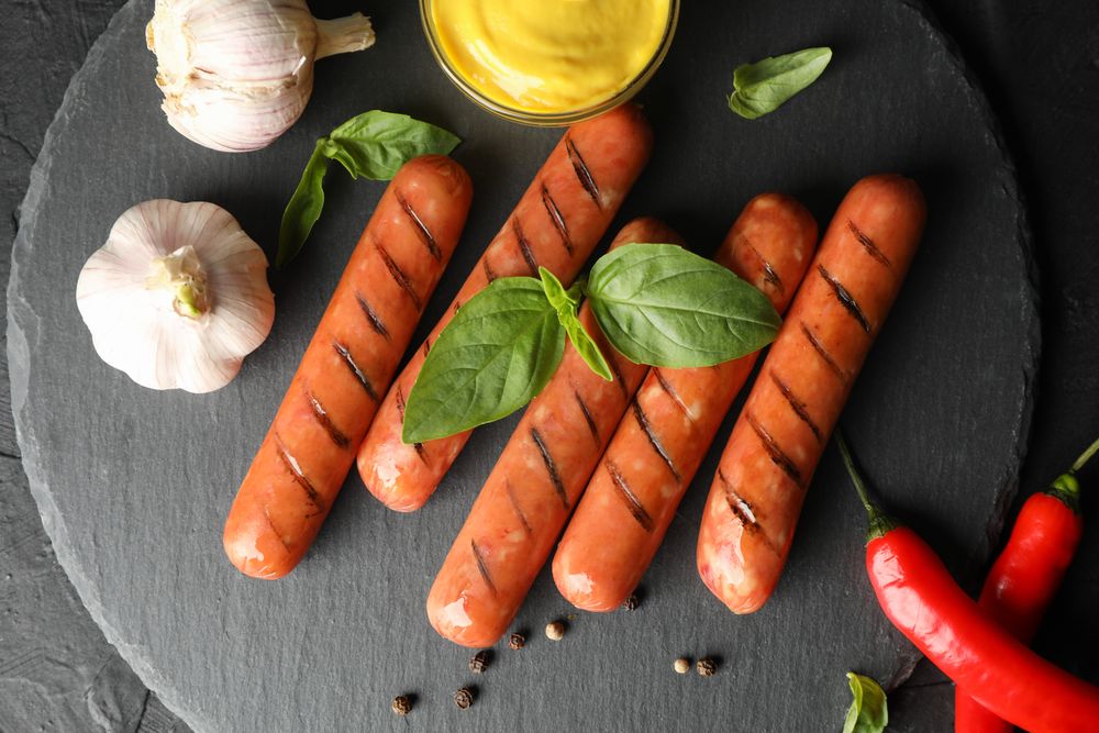Looking down at grilled sausages or hot dogs on dark ceramic plate with garlic and mustard