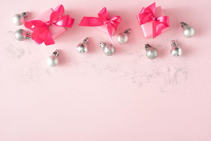 Gift boxes with pink ribbons on baby pink background and festive baubles
