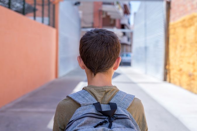 Back of boy wearing backpack walking in alley