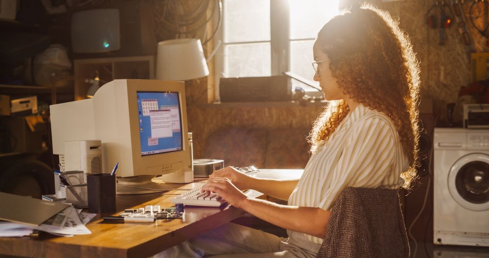 Side View Of Hispanic Female Software Engineer Programming on Old Desktop Computer In Retro Garage.