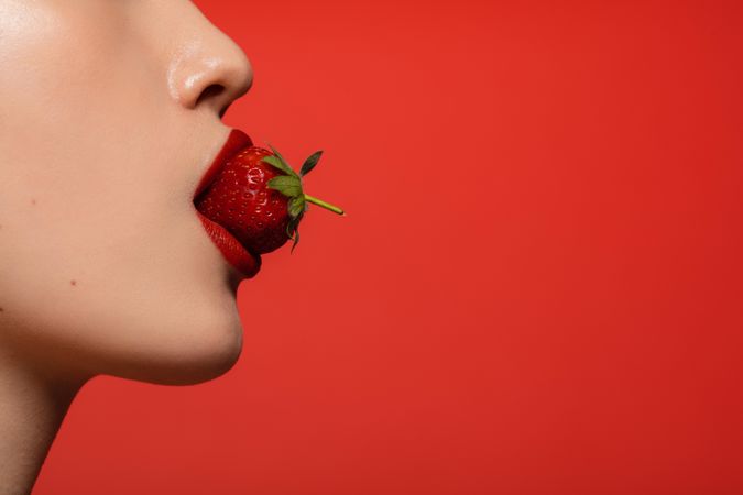 Woman with red lipstick eating a fresh strawberry